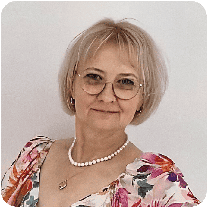 Anna Małgorzata Piotrowska - kobieta o krótkich blond włosach, w okularach i kwiecistej sukience uśmiecha się do aparatu. Ma na sobie kolczyki w kształcie kółek, naszyjnik z pereł oraz naszyjnik z zawieszką i stoi na jednolitym tle.