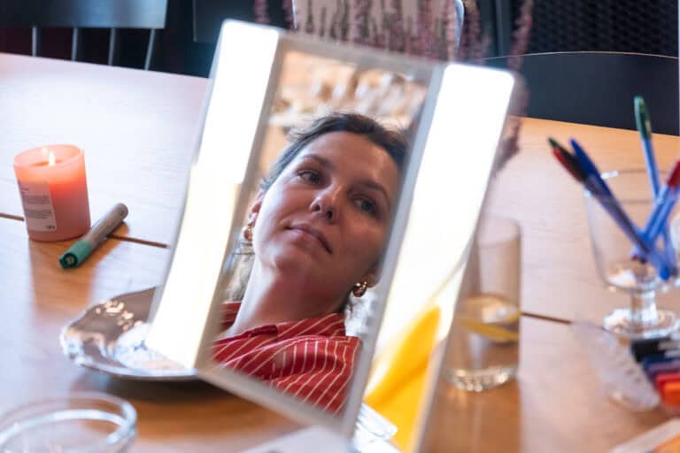 Kobieta widoczna w lusterku kosmetycznym stojącym na drewnianym stoliku.